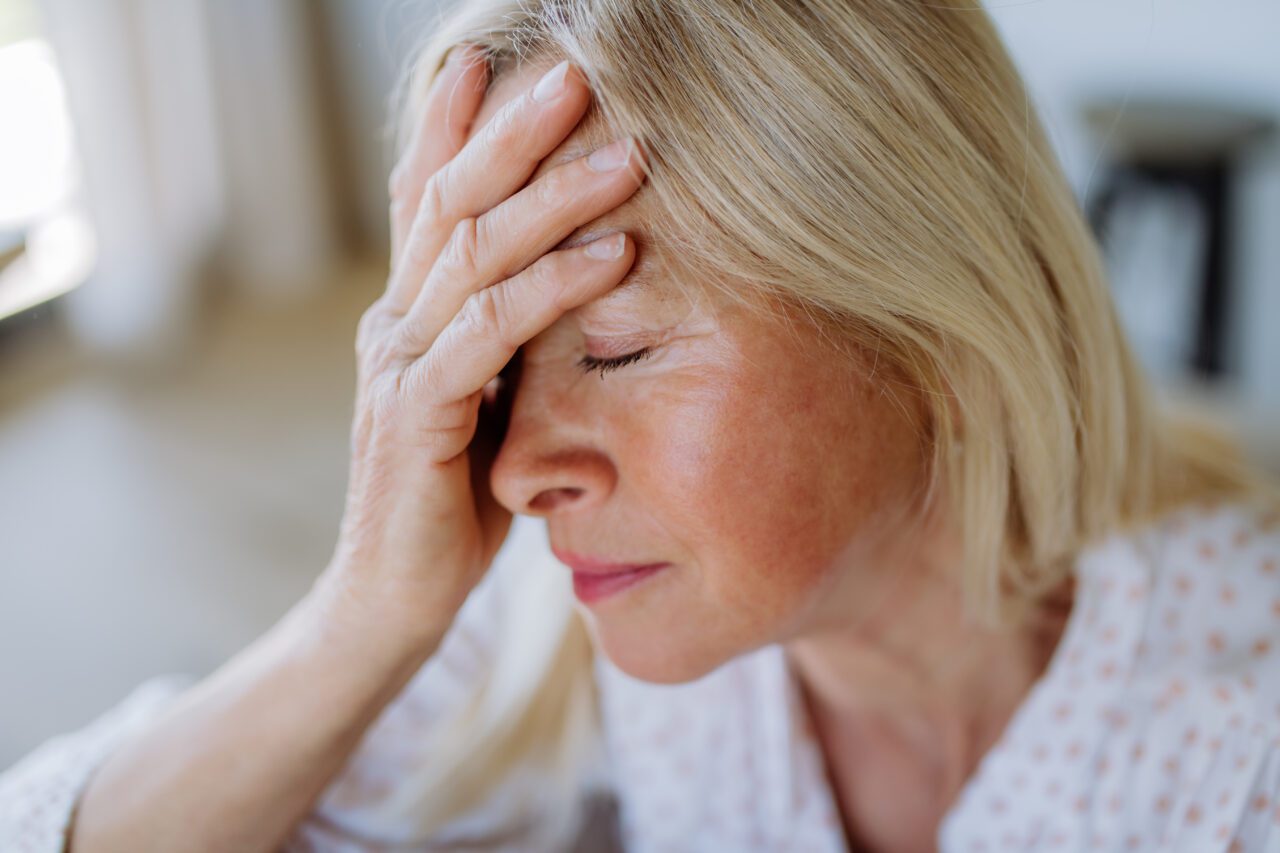 Portrait of an attractive senior woman sitting on a sofa at home with a headache